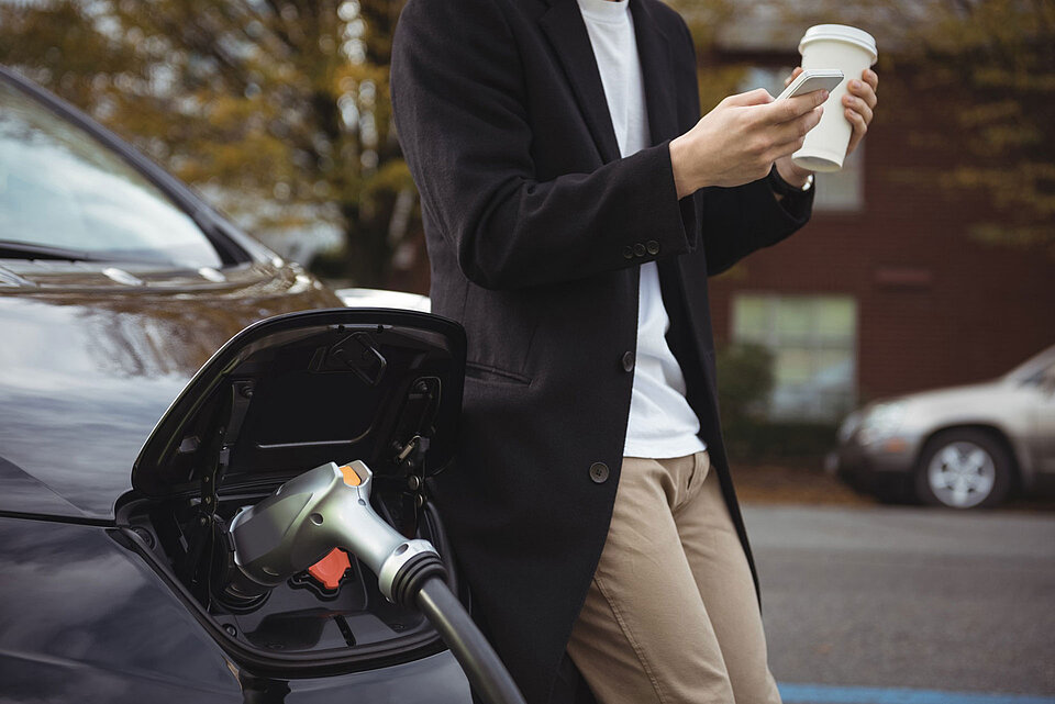 Ein Mann mit einem Kaffee in der Hand an seinem Auto angelehnt